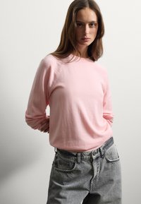 Hellrosa Strickpullover mit Rundhalsausschnitt und langen Ärmeln, kombiniert mit hochgeschnittenen grauen Jeans aus Denim mit lockerer Passform.