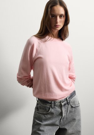 Lichtroze gebreide trui met een ronde hals en lange mouwen, gecombineerd met hooggetailleerde grijze denim jeans met een relaxte pasvorm.