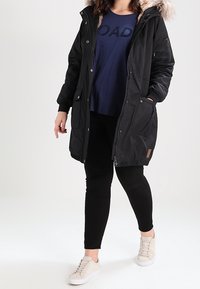 Černá parka s kapucí z umělé kožešiny, zipovým a knoflíkovým zapínáním, bočními kapsami a elastickým pasem. V kombinaci s námořnickou košilí a černými kalhotami.