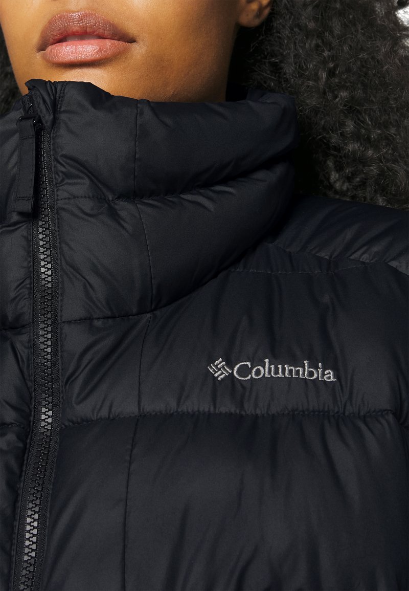 Chaqueta de plumas negra con collar alto, cierre de cremallera y logo de Columbia en el pecho. Textura suave, diseño acolchado y voluminoso.