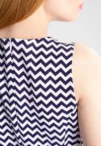 Robe sans manches avec un motif en chevrons bleu marine et blanc, dotée d'une fermeture éclair visible à l'arrière et d'un tissu texturé.