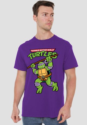 Lila Baumwoll-T-Shirt mit einem Grafikdesign eines grünen Schildkrötencharakters, der eine Waffe hält, und dem Text "Teenage Mutant Ninja Turtles" darüber.