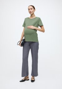 Πράσινο βαμβακερό t-shirt, άνετη εφαρμογή. Γκρι παντελόνι με φαρδιά μπάσκα, λεία υφή. Μαύρα επίπεδα παπούτσια με λουριά στον αστράγαλο. Απλή μαύρη τσάντα χειρός.