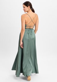 Lang, grünes Satin-Kleid mit fließender Silhouette. Verfügt über ein gekreuztes Rückendesign und anpassbare Bindetails. Glatte Textur, eleganter Fall.