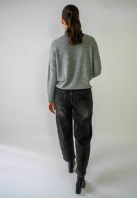 Grijze gebreide trui en hooggerokte vervaagde zwarte jeans. De jeans hebben achterzakken. Zwarte haklaarzen maken de outfit compleet.