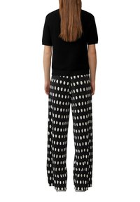 Czarna bluzka z krótkim rękawem zestawiona z czarnymi spodniami plisowanymi w dużą białą kropkę dla mocnego kontrastu.