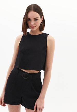 Black cropped top with a round neckline and fitted design, paired with high-waisted black shorts featuring a belt with a circular buckle.