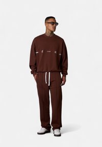 Brown sweatshirt with white text, relaxed fit, paired with matching brown sweatpants featuring white drawstring and side piping details.
