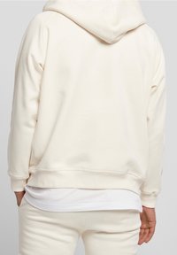 Sudadera beige clara hecha de tela suave, con un bolsillo tipo canguro y puños acanalados, de corte holgado y con capucha.