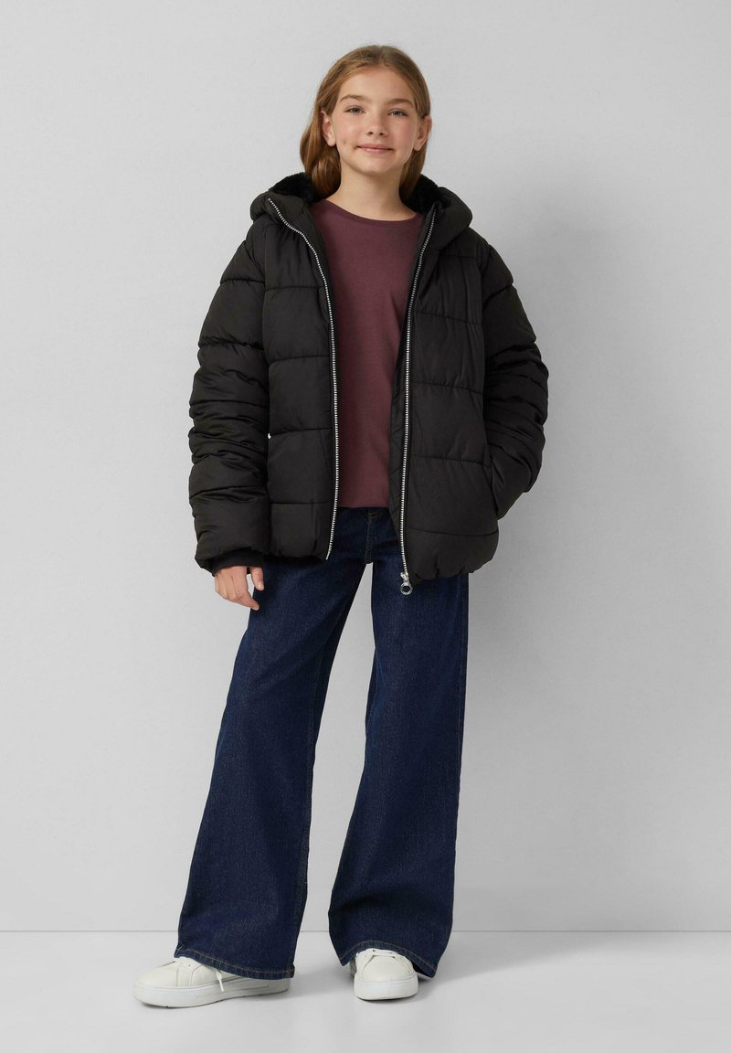 Crna jakna od puf materijala s kapuljačom, s kockastim dizajnom i prednjim zatvaračem. Uparena s bordo majicom i širokim tamnim trapericama.