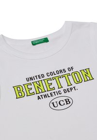 Maglietta bianca in cotone con collo rotondo. Presenta una grafica prominente in nero e giallo brillante, con il marchio "BENETTON" e "UCB".
