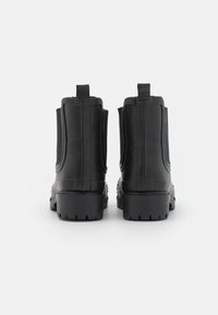 Bottes de cheville en caoutchouc noir avec une surface texturée, des panneaux latéraux élastiques et une semelle épaisse à motif. Deux languettes à l'arrière.