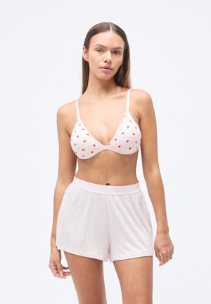 Bralette rose clair avec imprimé de cœurs rouges et bords festonnés, assorti à un short ample rose clair. Texture de tissu doux.