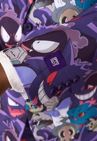 Fialový blazer so grafickou potlačou kreslených postáv, s bielou podšívkou a fialovými gombíkmi. Štítok označuje "OPPO SUITS."