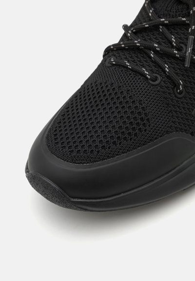 Svart sneaker med et teksturert mesh-overdel, forsterket tåhette og glatt gummisåle med kontrasterende snørebånd.