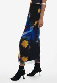 Colorful, floor-length skirt in a flowing fabric featuring vibrant abstract patterns. Paired with black sock-style heels.