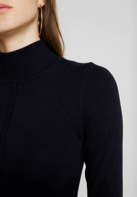 Granatowy sweter z golfem w prążki, posiadający wysoki kołnierz, teksturowane rękawy i subtelne szwy na ramionach. Gładka dzianina z dopasowanym krojem.