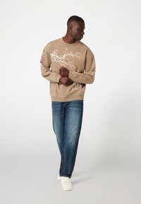 PUPAVO spalvos džemperis su gėlių raštu, derinamas su mėlynomis džinsomis ir baltais sportbačiais. Džemperis turi ilgomis rankovėmis ir apvaliu iškirpimu.