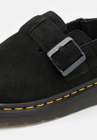 Czarne zamszowe buty z okrągłym noskiem, z metalową klamrą, żółtym szyciem wokół podeszwy oraz teksturowaną gumową podeszwą.