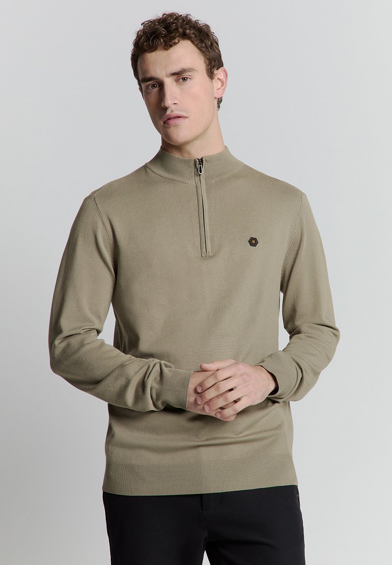 Beige zip-up trui met een hoge kraag, ribbelstructuur, lange mouwen en een subtiel embleem op de borst. Soepele, aansluitende pasvorm.