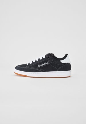 Czarne zamszowe sneakersy z białymi sznurówkami i logo, z białą podeszwą środkową i brązową gumową podeszwą. Klasyczny design z przeszyciami.