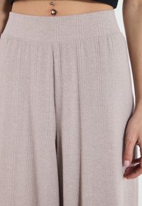 Světle šedé široké kalhoty s žebrovaným vzorem, elastickým pasem, vertikální strukturou a jemnými záhyby na přední straně.