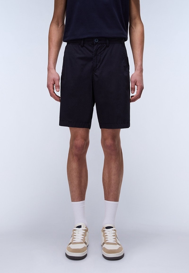 Shorts noirs, tissu léger, coupe droite, longueur genou. Associés à des baskets beige et blanches, avec un design à lacets et des semelles texturées.