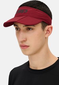 Maroon sports visor with adjustable band, featuring a wide brim and black logo detail. Lightweight fabric, designed for comfort and ventilation.