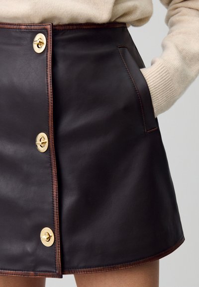 Gonna in pelle marrone dal taglio dritto, con chiusura centrale a bottone, tasche laterali e cuciture a contrasto lungo i bordi.
