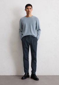 Lichtblauwe trui met een ronde hals, gecombineerd met donkerblauwe broek. De outfit wordt aangevuld met zwarte veterschoenen.