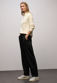 Kość słoniowa prążkowany sweter z wysokim kołnierzem, w połączeniu z czarnymi luźnymi spodniami z bocznymi paskami i beżowymi trampkami.