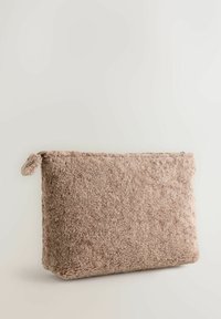 Struktureret beige taske lavet af blødt, fluffy materiale. Rektangulær form med lynlåslukning og et lille loopet håndtag.