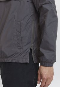 Gray windbreaker jacket with a side zipper and elastic cuffs. Features a smooth texture, slightly loose fit, and a side pocket.