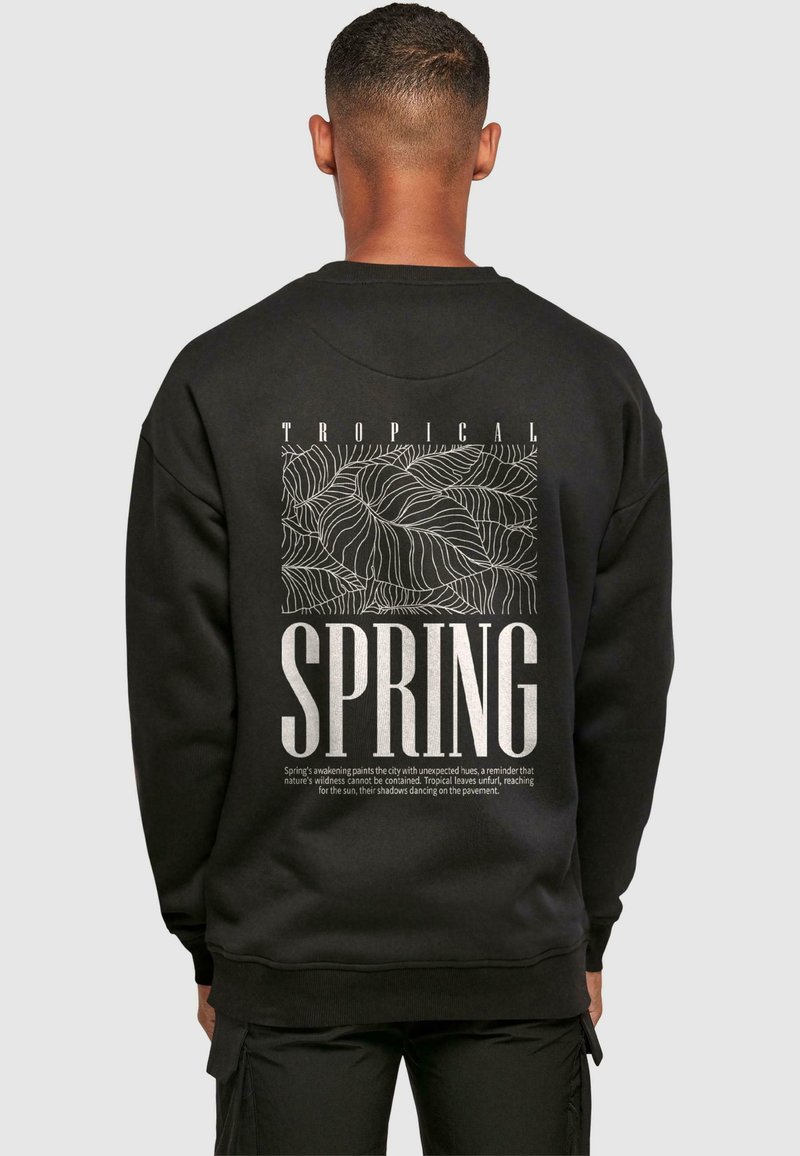 Mustaline särk, millel on valge graafiline disain, millel on tekst "TROPICAL SPRING" ja lehe mustrid seljal. Pehme tekstuur, ümmargune kaelus.