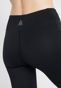 Leggings de sport noirs en tissu extensible, dotés d'une taille haute avec le logo Reebok et de coutures plates et nettes pour une finition lisse.