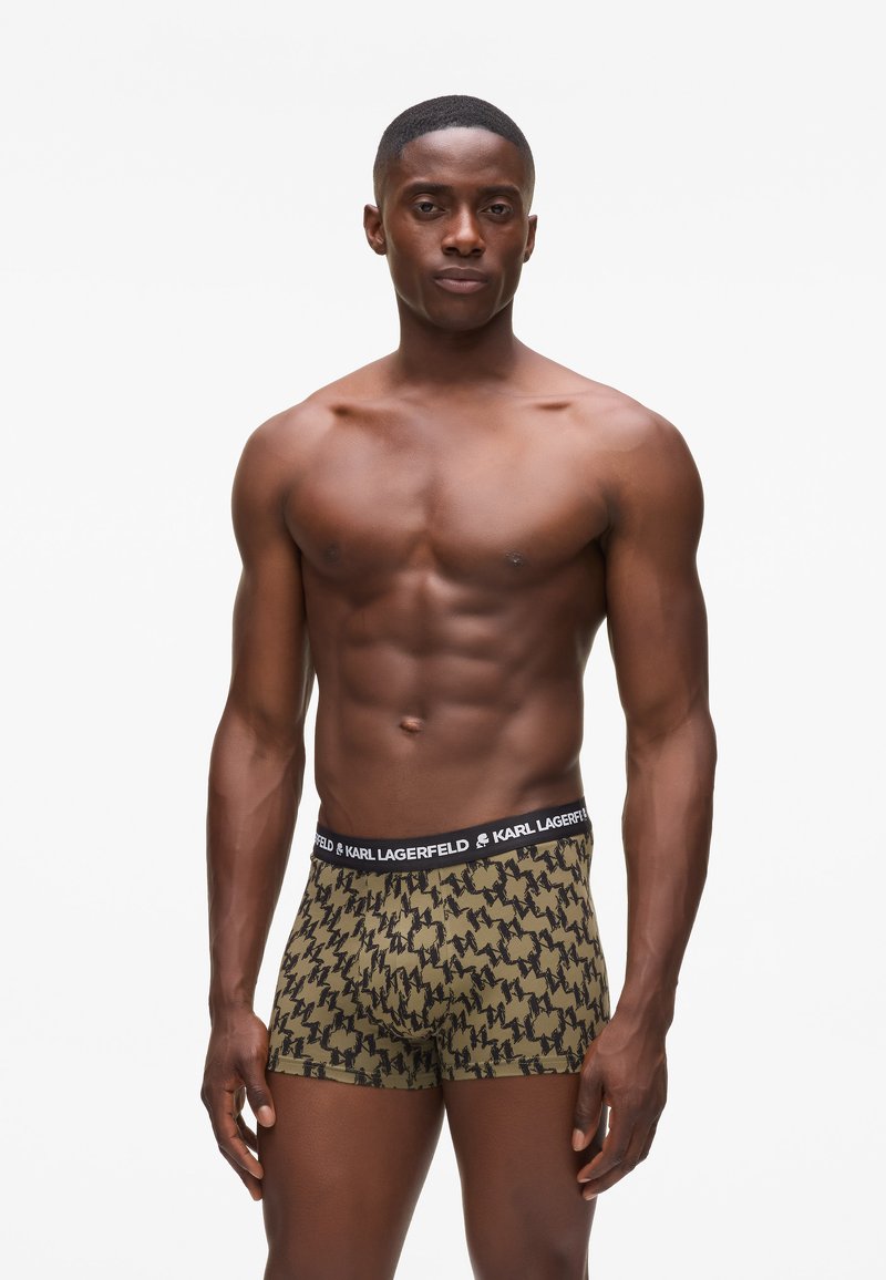 Boxers en verde oliva con un patrón de rayo negro. Presentan una cinturilla negra con el logo "KARL LAGERFELD". Tejido suave y diseño ajustado.