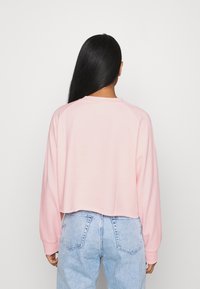 Felpa cropped rosa con maniche raglan lunghe, polsini a coste e una texture morbida, abbinata a jeans azzurri a vita alta.