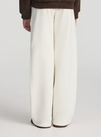 Pantaloni bianchi a gamba larga realizzati in tessuto morbido, caratterizzati da una texture liscia e un design semplice. La vita è elastica, garantendo comfort.