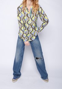 Värikäs, pitkähihaisempi paita, jossa on aalto-kuvio vihreänä, sinisenä ja ruskeana. Yhdistetty vaaleansinisiin, kuluneisiin leveälahkeisiin farkkuihin ja tennareihin.