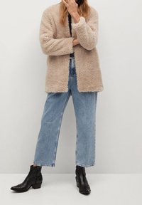 Beige faux fur jakke med en afslappet pasform, åben front, parret med lyseblå brede bukser og sorte læder ankelstøvler.