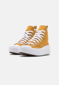Zapatillas altas de ante amarillo mostaza con cordones blancos, suela gruesa blanca y suela de goma marrón; cuenta con una lengüeta en la parte trasera.