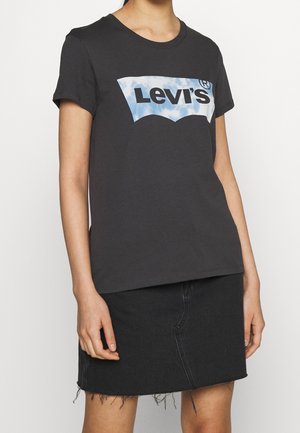 Czarna bawełniana koszulka z krótkim rękawem, z niebiesko-białym logo Levi's w zaokrąglonym kształcie na klatce piersiowej. Nosi ją czarna dżinsowa spódnica.