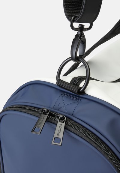 Mochila azul-marinho com um detalhe branco, fabricada com um material liso e flexível, puxadores de zíper pretos e hardware de alças ajustáveis.