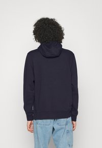 Mörkblå huvtröja med dragsko i huvan, långa ärmar och ribbstickade muddar. Tillverkad av mjukt tyg med en enkel, ren design.