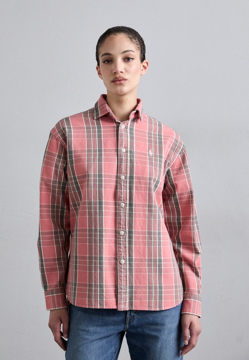 Camisa de cuadros rosa con acentos en gris y blanco, frente abotonado, mangas largas y un logo en el lado izquierdo del pecho. Diseño casual y material de algodón.