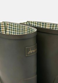 Tmavo zelené gumové čižmy do dažďa s textúrovaným povrchom, s podšívkou s károvaným vzorom v zelenej a bielej farbe a zlatou logo nášivkou.