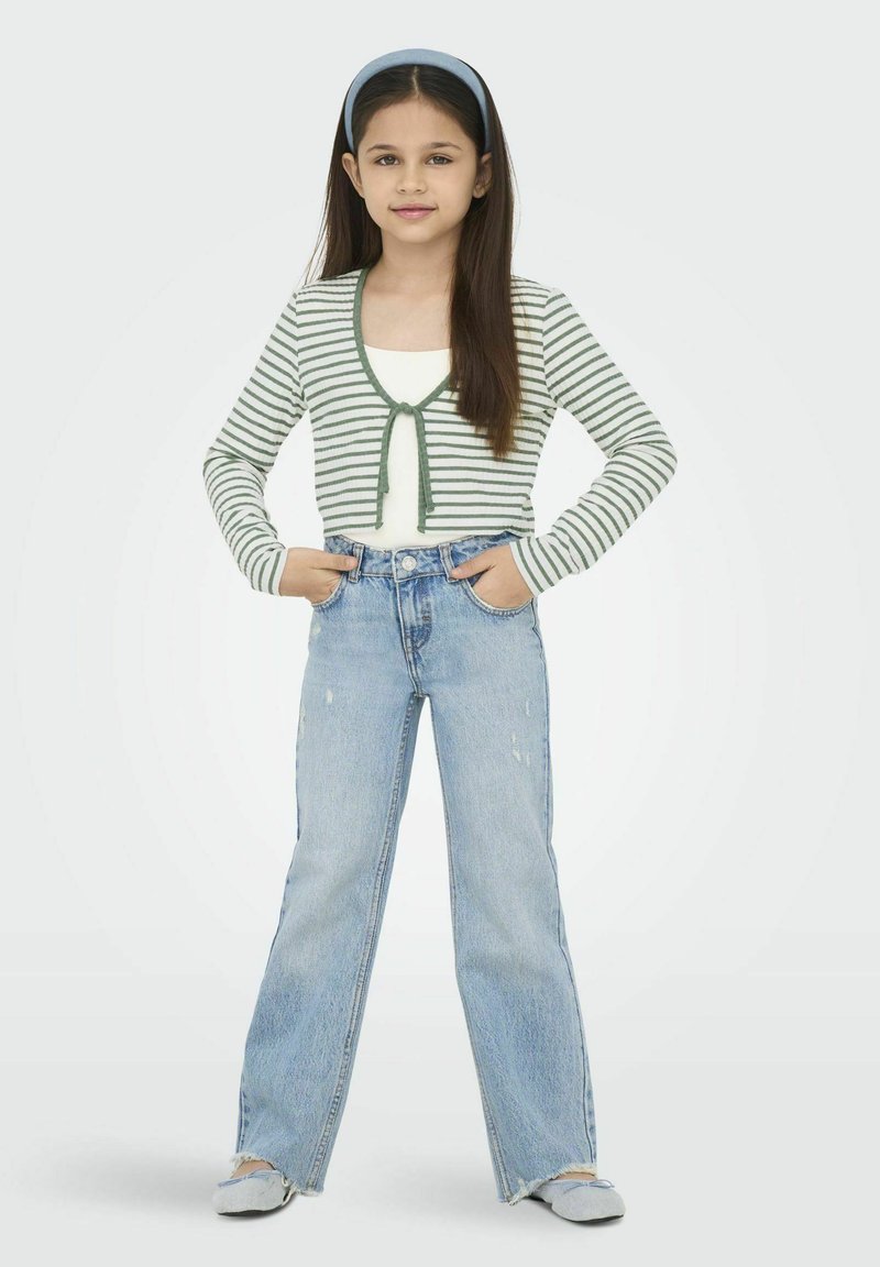 Gestreepte groene en witte cropped cardigan met een strik, gedragen over een witte top. Ruime lichtblauwe jeans met versleten details en grijze schoenen.