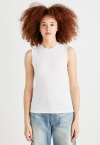 White sleeveless top made of smooth fabric with a fitted design, featuring a round neckline and no visible fastenings, paired with light blue jeans.