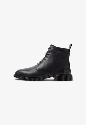 Stivaletto alla caviglia in pelle nera con allacciatura frontale e suola strutturata e scanalata, visto di lato su sfondo bianco.
