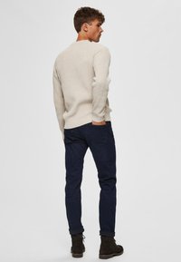 Beige ribbed sweater and dark blue jeans, with a fitted silhouette and textured fabric. Features ankle boots and a simple design.